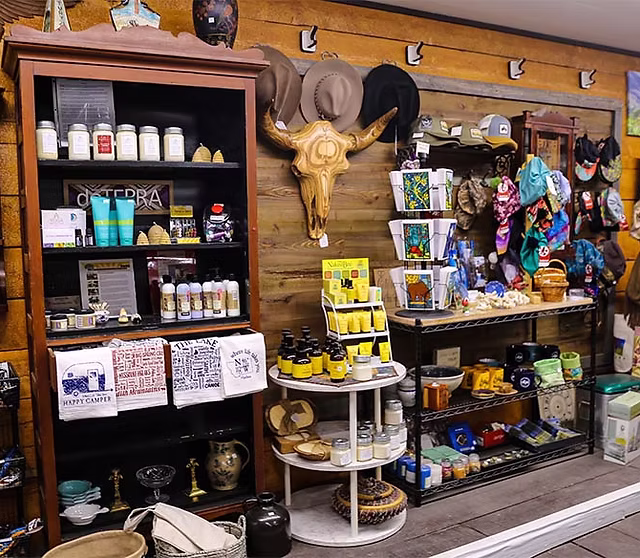 Trading post interior showing various goods including local honey, hats, candles, and handmade tote bags