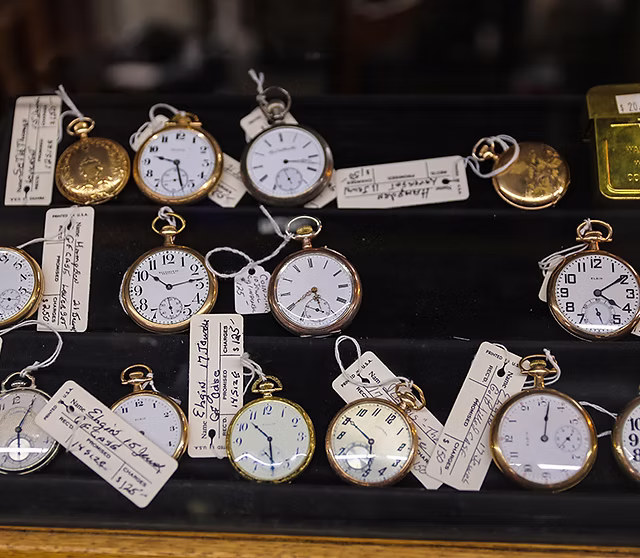 A collection of antique gold and silver pocket watches with original price tags on a display tray